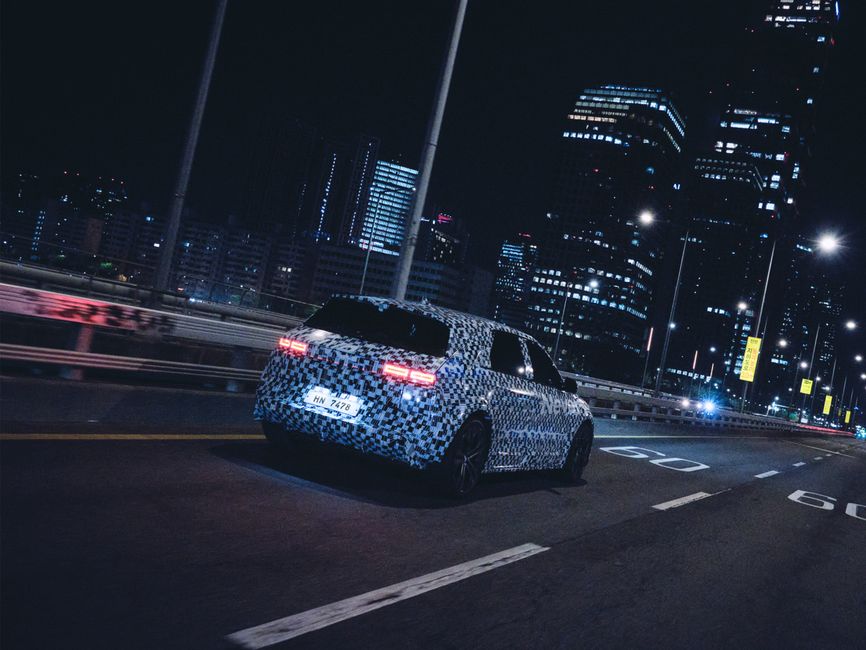 Electric vehicle with camo wrap driving through illuminated city at night, showcasing futuristic car design.