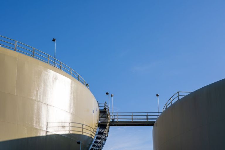 Sunlit industrial silos connected by a staircase under a clear blue sky.