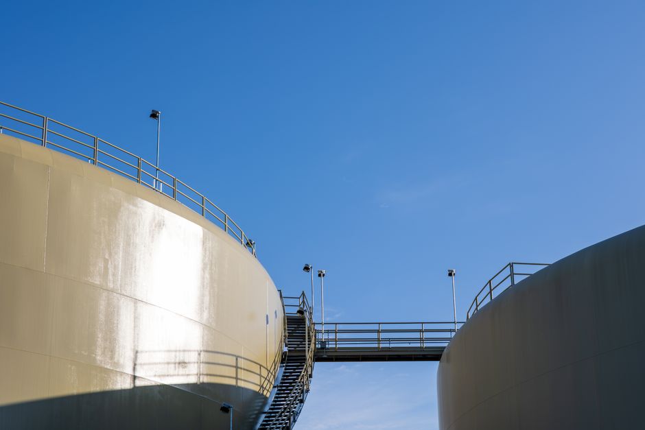 Sunlit industrial silos connected by a staircase under a clear blue sky.