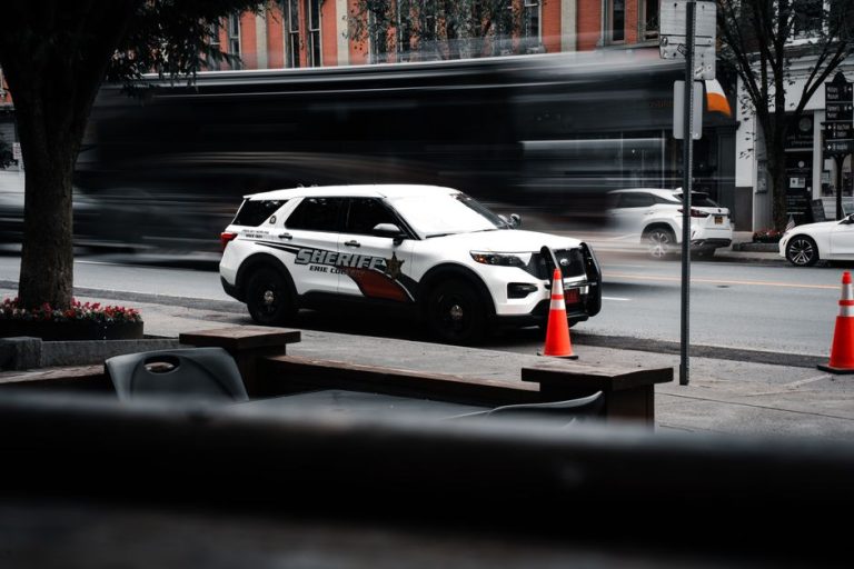 Sheriff's vehicle parked on a bustling city street with traffic motion blur.