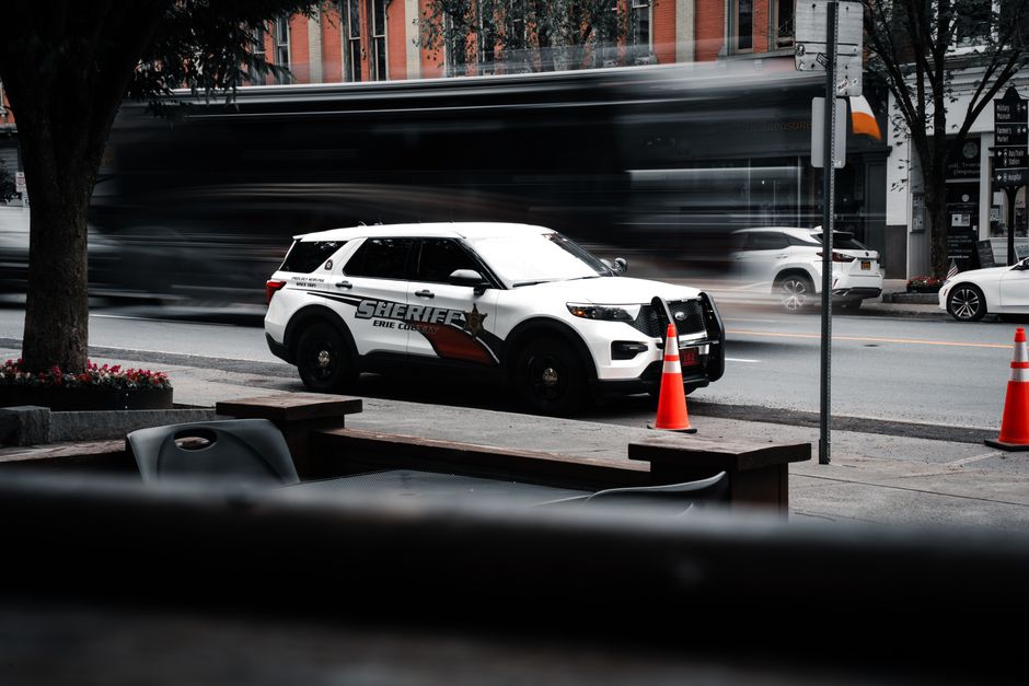Sheriff's vehicle parked on a bustling city street with traffic motion blur.