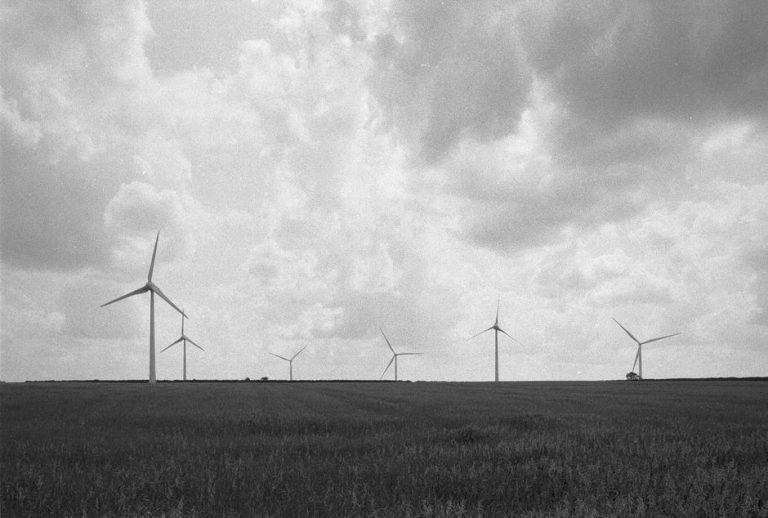 Black and white photo of wind turbines standing in a vast rural meadow under a cloudy sky.