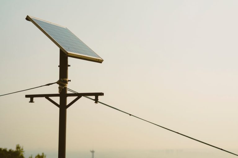 A single solar panel mounted on a tall post against a clear sky, symbolizing renewable energy.