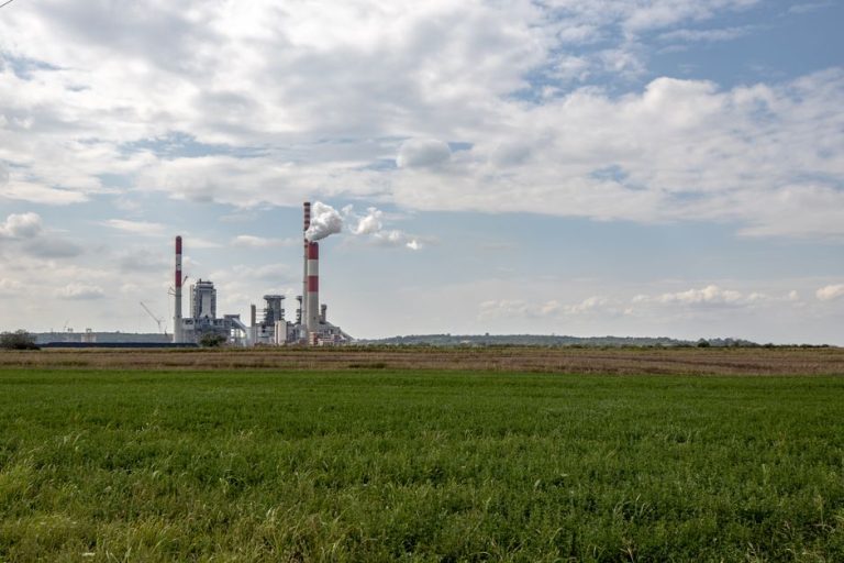 Thermal power plant with smokestacks emitting in Serbia's rural landscape.