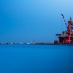 A vibrant offshore oil rig with large cranes at a busy sea port during the day.