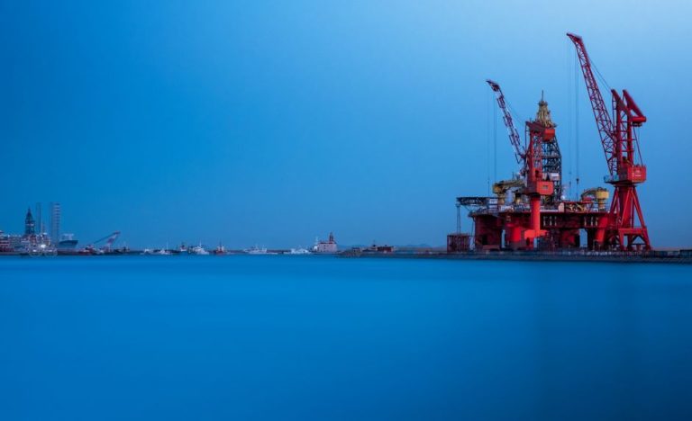 A vibrant offshore oil rig with large cranes at a busy sea port during the day.