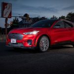 Red Ford Mustang Mach-E electric SUV parked at night in an urban setting.
