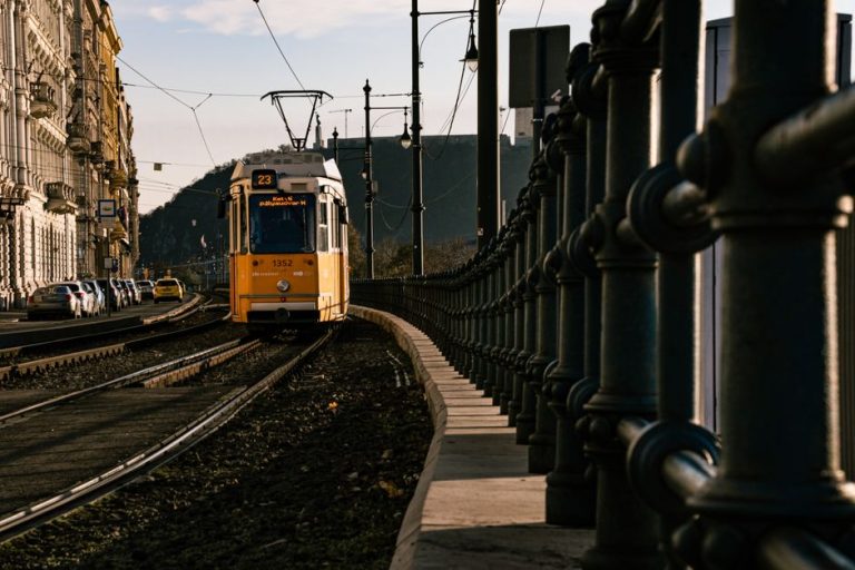 A classic yellow tram travels through the urban streets of Budapest, captured in the warm glow of autumn.