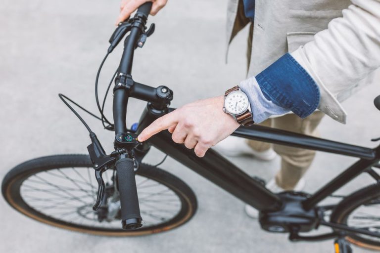 Caucasian man with a wristwatch touches the screen on a black electric bicycle, showcasing modern technology in transportation.