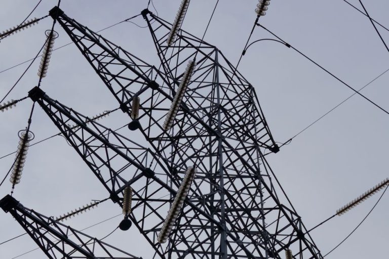 Low angle shot of a metal power transmission tower with cables against a clear sky.