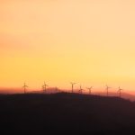 Silhouette of wind turbines at sunset, promoting sustainable energy.