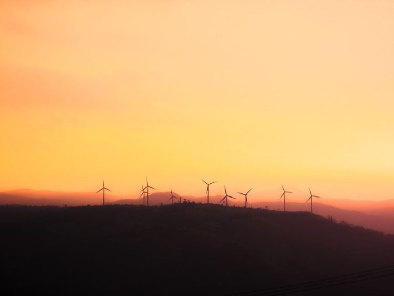 Silhouette of wind turbines at sunset, promoting sustainable energy.