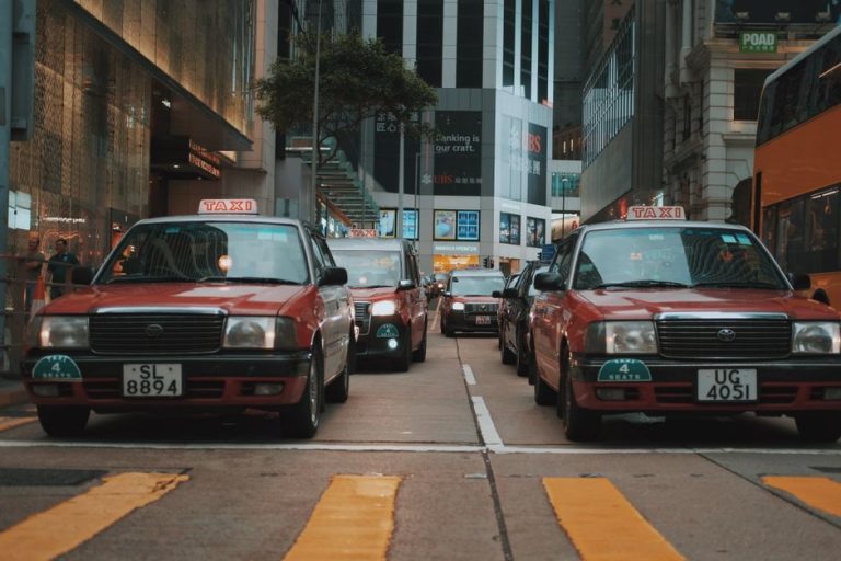 Red taxis driving through a busy downtown street in Hong Kong, showcasing urban life and vibrant city atmosphere.