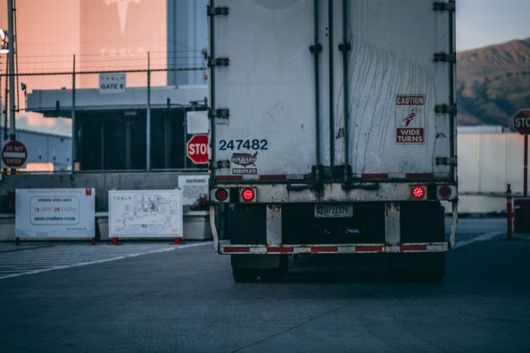 Semi truck parked at a loading dock with visible caution signs and industrial surroundings.