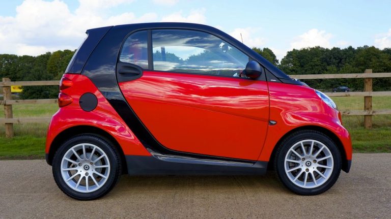 Red Smart Fortwo car parked on a countryside road with a scenic background.