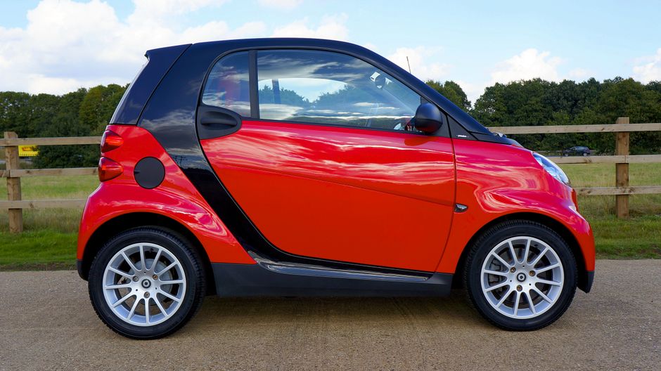 Red Smart Fortwo car parked on a countryside road with a scenic background.