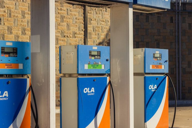 Three blue OLA Energy gas pumps at an outdoor station on a sunny day.