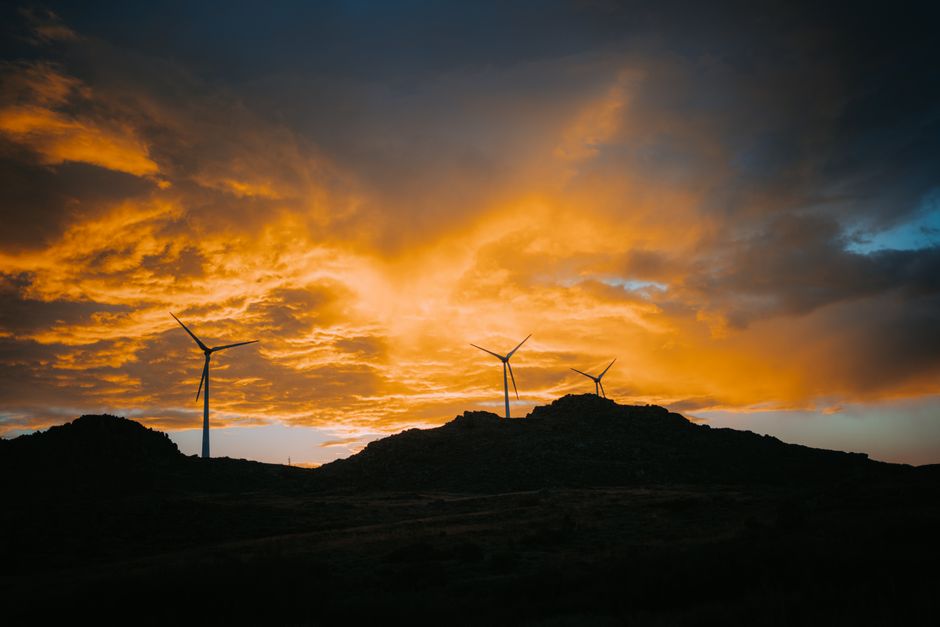 Three wind turbines silhouetted on a hill at sunset, showcasing renewable energy on a dramatic landscape.