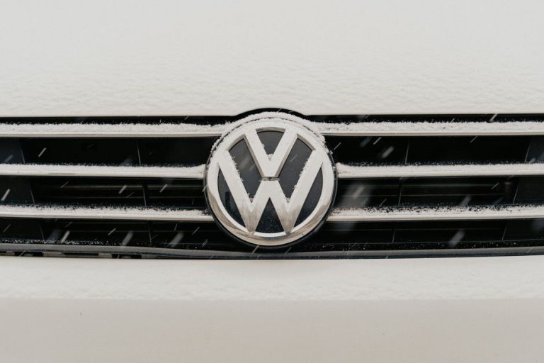 Closeup of a snow-dusted Volkswagen car grille shows the iconic VW logo.