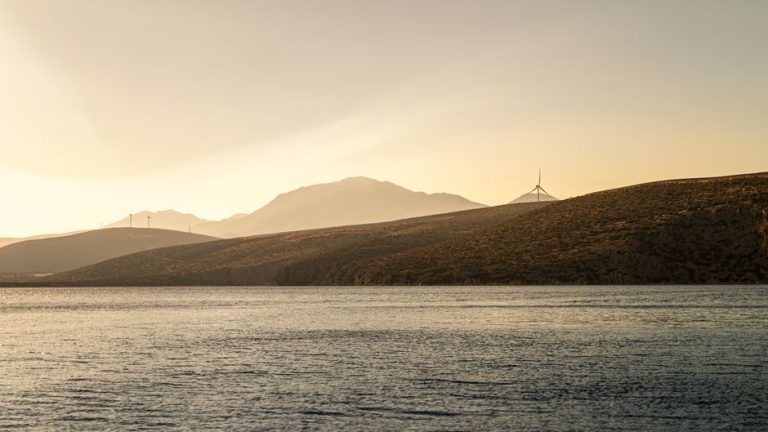 Peaceful coastal view of wind turbines at sunset in Greece, showcasing clean energy and scenic beauty.
