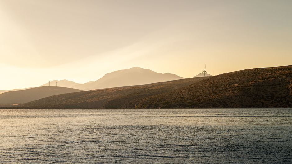 Peaceful coastal view of wind turbines at sunset in Greece, showcasing clean energy and scenic beauty.