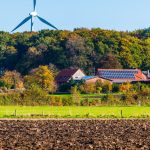 A picturesque sustainable farm featuring wind turbine and solar panels surrounded by vibrant autumn foliage.