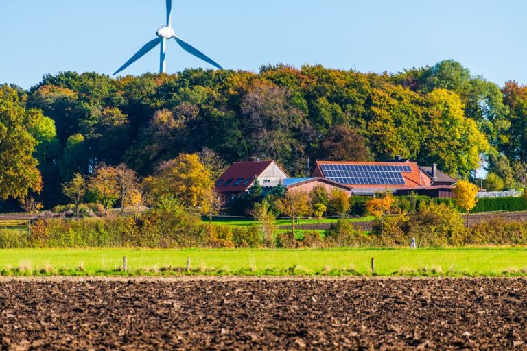 A picturesque sustainable farm featuring wind turbine and solar panels surrounded by vibrant autumn foliage.