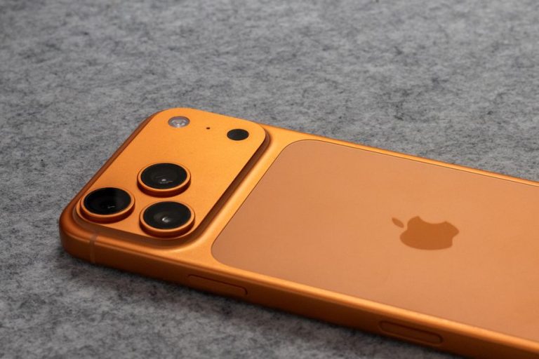 Orange smartphone with dual cameras placed on a soft gray fabric surface.