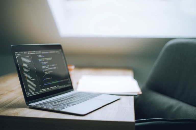 Open laptop displaying code on desk in bright, modern office setting. Ideal for tech and remote work context.