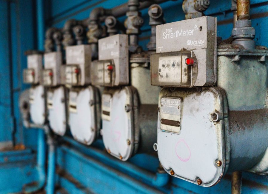 Multiple smart utility meters lined up on a blue industrial wall.