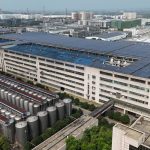 Aerial view of a modern industrial building with solar panels and storage tanks.