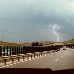 Dramatic lightning storm over a picturesque highway, captured from a moving car.