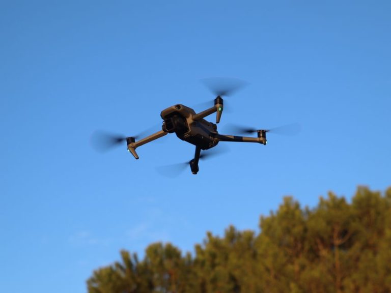A drone hovering outdoors in daylight with motion-blurred propellers against a blue sky in Valladolid, Spain.