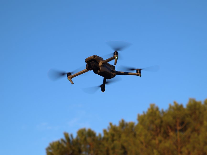 A drone hovering outdoors in daylight with motion-blurred propellers against a blue sky in Valladolid, Spain.