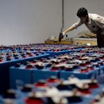 A worker checking many industrial batteries inside a facility. Indoor, industrial setting.