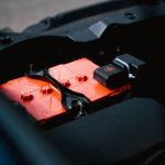 Detailed view of an orange car battery inside a vehicle's engine bay, highlighting its features.