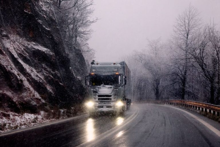 Heavy truck driving through snowy mountain road during winter snowfall.