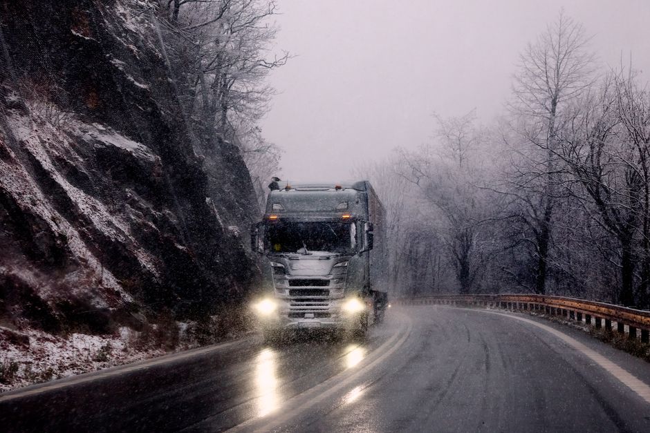 Heavy truck driving through snowy mountain road during winter snowfall.
