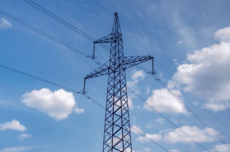 A high voltage transmission tower set against a bright blue sky with scattered clouds, showcasing modern infrastructure.
