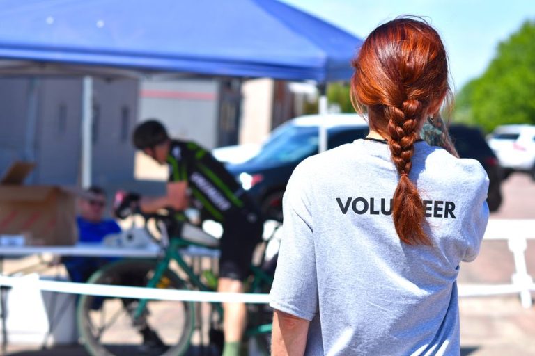 A volunteer oversees a charity bike event under a blue tent on a sunny day.