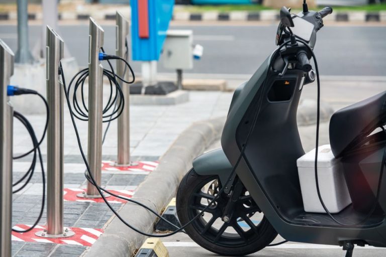 Electric scooter plugged into a charging station in a city environment, showcasing eco-friendly urban transportation.