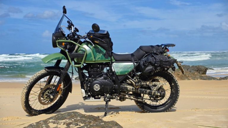 Green adventure motorcycle parked on Cooloola Beach, Queensland, Australia under a clear blue sky.