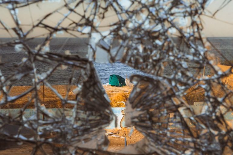 A unique view of a coastal campsite through shattered glass, capturing a sense of adventure.