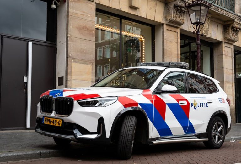 A Dutch police car parked on an Amsterdam street in front of a historic building.