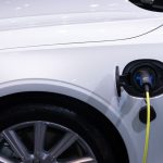 A white electric car is plugged in for charging, close-up view of the charging port.