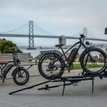Electric bicycles parked near the iconic San Francisco Bay Bridge on a cloudy day.