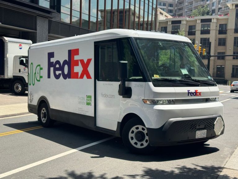 Electric FedEx delivery truck parked on an urban street in daylight.