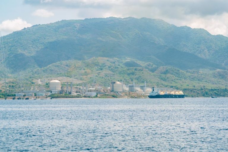 Coastal industrial facility with a tanker ship against a mountainous backdrop.