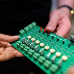 Close-up of hands holding a green circuit board used for electronic projects.