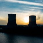 Identical cooling tower silhouettes on power plant near rippled river under colorful cloudy sky at sundown